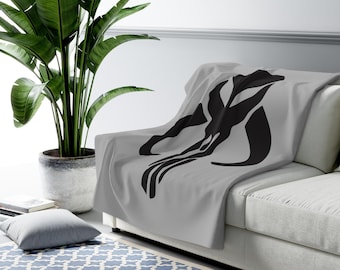 May include: A gray fleece throw blanket with a black Mandalorian symbol printed on it. The blanket is draped over a white couch.