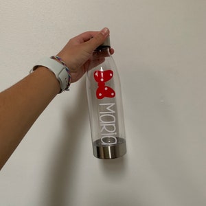 K&ouml;nnte beinhalten: Eine durchsichtige Wasserflasche aus Plastik mit einem silbernen Deckel und einer roten Schleife mit wei&szlig;en Punkten. Auf der Flasche steht der Name "Maria" in wei&szlig;.