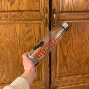 May include: A clear glass water bottle with a black heart and the name "Maria" in red lettering.