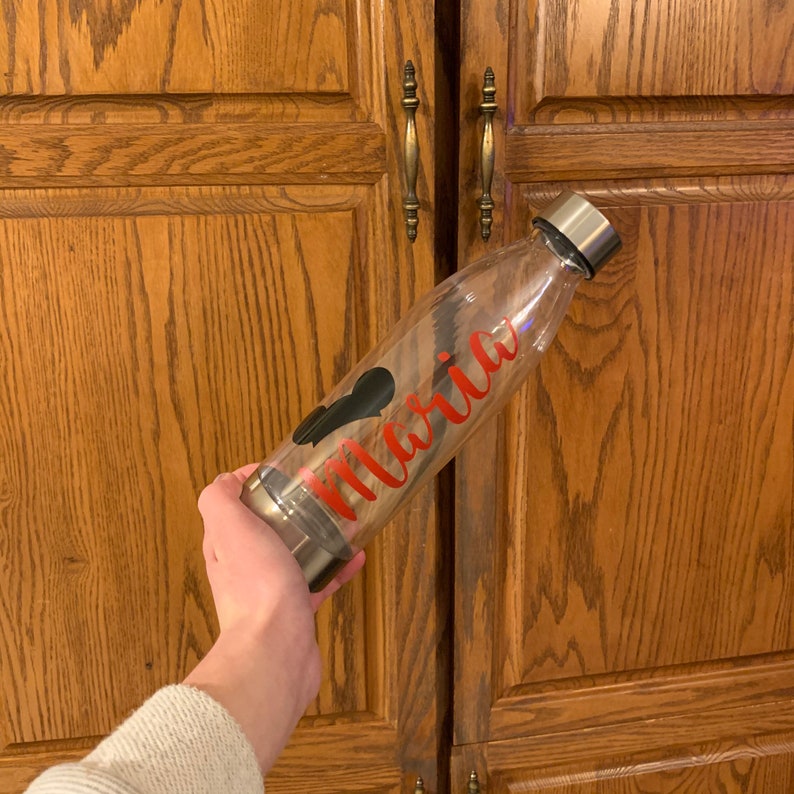 May include: A clear glass water bottle with a black heart and the name "Maria" in red lettering.