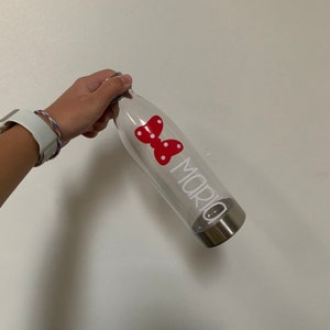 K&ouml;nnte beinhalten: Transparente Wasserflasche aus Plastik mit einem roten Schmetterlingsaufkleber und dem Namen "Maria" in wei&szlig;. Die Flasche hat einen silbernen Deckel.