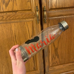 May include: A clear glass water bottle with a black heart and the name "Maria" written in red lettering.