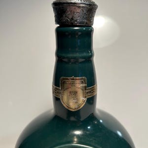 May include: A green ceramic bottle with a silver cap. The bottle has a label that reads "Chivas Brothers Ltd.  Aberdeenshire, Scotland". The bottle also has a label that reads "Royal Salute 21".