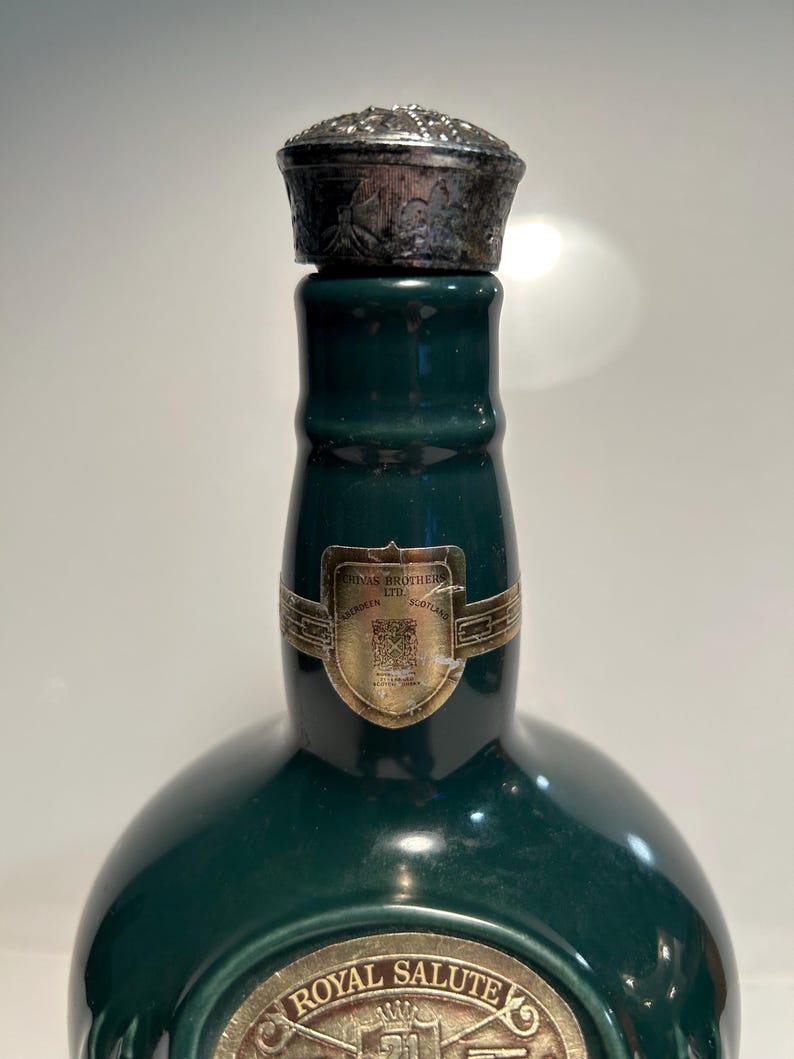 May include: A green ceramic bottle with a silver cap. The bottle has a label that reads "Chivas Brothers Ltd.  Aberdeenshire, Scotland". The bottle also has a label that reads "Royal Salute 21".