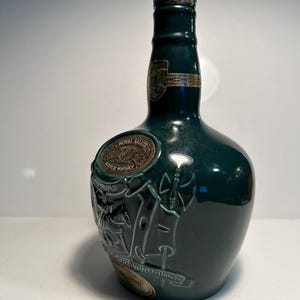 May include: A green ceramic bottle of Royal Salute Scotch Whisky. The bottle has a silver cap and a gold label with the words "Royal Salute" and "Scotch Whisky".
