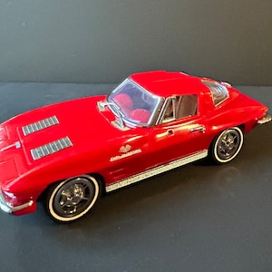 May include: A red model car with a hardtop. The car features silver trim, black wheels with white sidewalls, and a detailed interior. The text "FUEL INJECTION" is visible on the side.