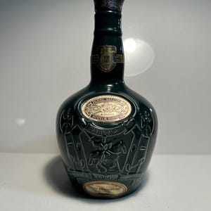 May include: A green ceramic bottle of Chivas Regal Royal Salute Scotch whisky. The bottle features a gold label with the words "Royal Salute" and "Scotch Whisky" and a crest with a knight on horseback. The bottle is embossed with a crest and the words "Chivas Brothers Ltd."