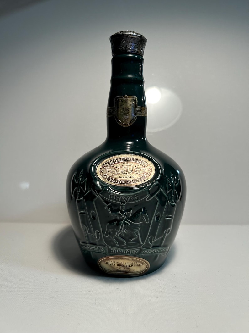 May include: A green ceramic bottle of Chivas Regal Royal Salute Scotch whisky. The bottle features a gold label with the words "Royal Salute" and "Scotch Whisky" and a crest with a knight on horseback. The bottle is embossed with a crest and the words "Chivas Brothers Ltd."