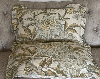 May include: Two decorative throw pillows with a floral pattern in shades of green, beige, and yellow. The pillows are on a gray couch.