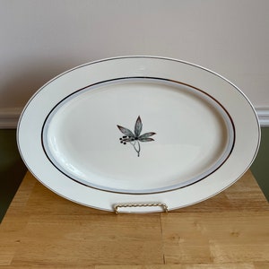 May include: White oval serving platter with a gold rim and a delicate green and brown leaf design in the center.