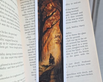 May include: Bookmark featuring a watercolor painting of a person in a carriage traveling down a path through a forest. The artwork has warm tones of orange, brown, and yellow, with dark tree silhouettes.