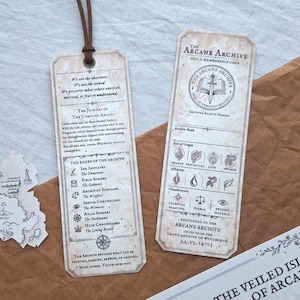 May include: Two rectangular paper bookmarks with aged parchment texture and dark brown text. One bookmark features a brown leather cord at the top, while the other is a membership card for The Arcane Archive, displaying various symbols and text.