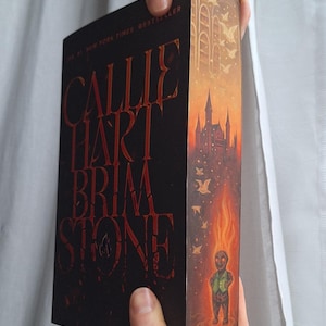 May include: A hardcover book titled "Callie Hart Brimstone" with red lettering on a black background. The spine features a castle illustration with a fiery figure. The book is a New York Times Bestseller.