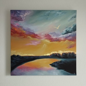 A painting on canvas of a colourful sky with pinks, purples, yellows and blues reflecting on a lake with gold foil along the horizon and a gold bird in the sky