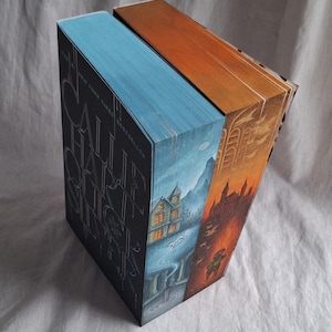 May include: Two hardcover books with illustrated edges. One book has a blue cover with silver lettering and a landscape illustration. The other book has an orange cover with a castle illustration. The books are titled "Call Hall Silver".