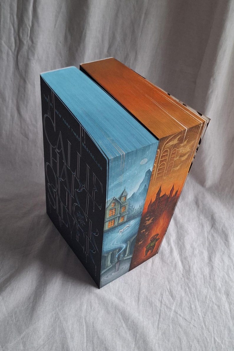 May include: Two hardcover books with illustrated edges. One book has a blue cover with silver lettering and a landscape illustration. The other book has an orange cover with a castle illustration. The books are titled "Call Hall Silver".