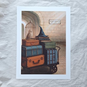 May include: A print depicting a luggage cart loaded with vintage suitcases in shades of orange, blue, and green. A cage with an owl sits atop the luggage. A wizard's hat and books are stacked next to the cage. The sign reads "Platform 9".