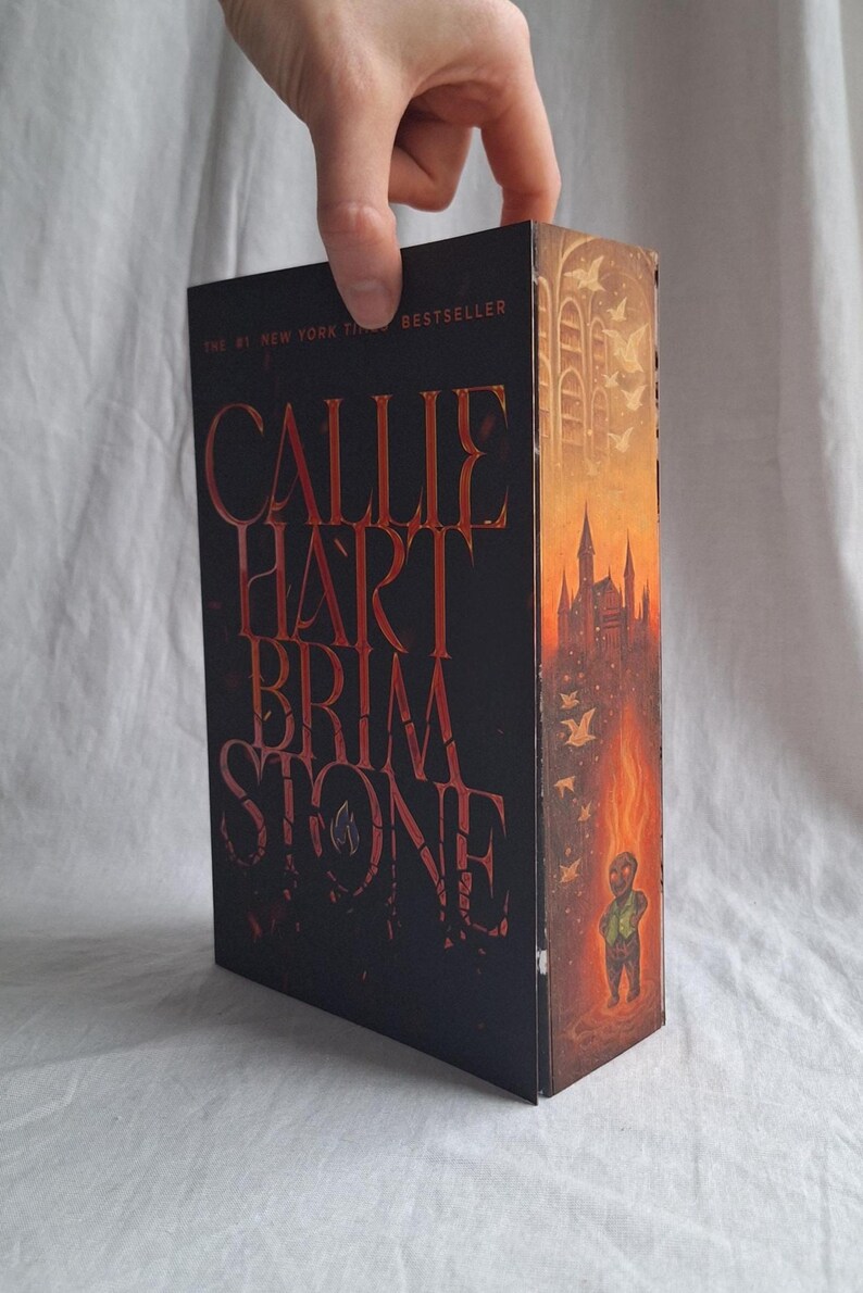 May include: A hardcover book titled "CALLIE HART BRIMSTONE" with a dark cover and red lettering. The spine features a castle illustration in shades of orange and yellow. The book is a New York Times bestseller.