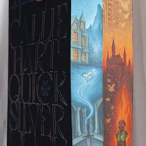 May include: A hardcover book titled "Quicksilver" by Callie Hart. The book's spine is black with silver lettering. The edges of the pages are painted with fantasy scenes in blue, orange, and brown tones, featuring a house, a fox, a sword, and a figure.
