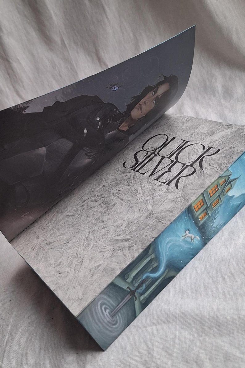 May include: Open book with the title "QUICKSILVER" in a stylized font. The cover features a woman in dark clothing, while the edges showcase a detailed illustration of a building and a swirling blue form.