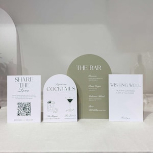 May include: A set of four wedding signage pieces including two rectangular white cards with black text, one arched white card with black cocktail illustrations and text, and one large arched sage green card with a white menu list titled THE BAR.