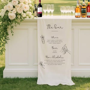 May include: A cream-coloured bar with a banner displaying "The bar" and drink options. Wine, beer, and non-alcoholic choices are listed. Wine bottles, glasses, and flowers are arranged on the bar.
