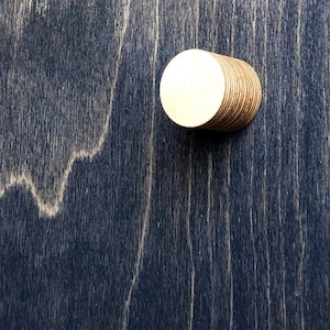 May include: A stack of round wooden discs, each with a smooth, light brown surface. The discs are stacked on top of each other to form a cylinder shape.