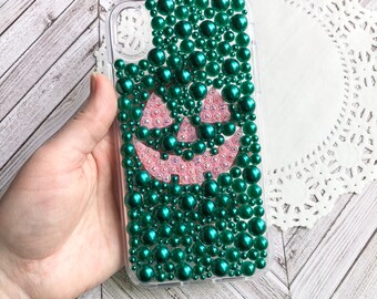 May include: A clear phone case decorated with green and pink beads in the shape of a jack-o'-lantern.