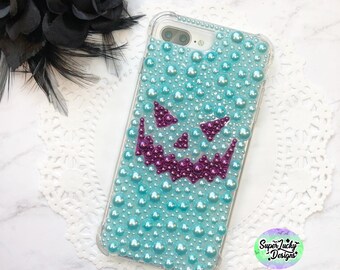 May include: A clear phone case with a turquoise and purple jack-o'-lantern design made of rhinestones. The case has a clear back and sides, and the design is visible through the case. The case is for an iPhone 7 Plus.