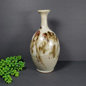 Könnte beinhalten: Eine Keramikvase mit brauner und weißer Glasur. Die Vase hat einen schmalen Hals und einen runden Körper.