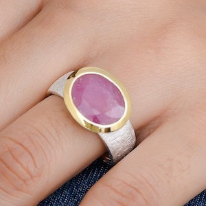 May include: A silver ring with a textured band and a gold setting. The ring features a large oval-shaped pink gemstone.