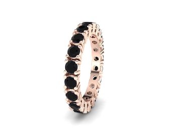 May include: Rose gold eternity ring with a continuous line of black gemstones. The ring's band has a warm, metallic hue, and the gemstones are round and evenly spaced, creating a symmetrical design. The ring is set against a white background.