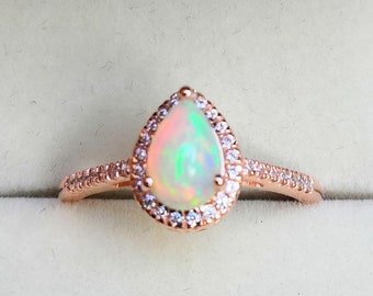 May include: A pear-shaped opal ring set in rose gold with a halo of small diamonds. The ring is in a white velvet ring box.