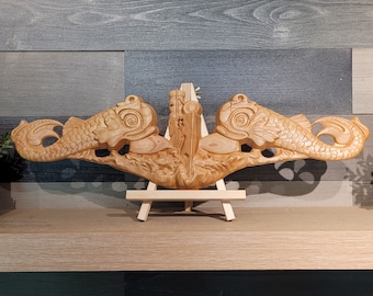 May include: A wooden sculpture of two dolphins facing each other, with intricate details and a natural wood finish. The sculpture is mounted on a small wooden easel.