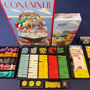 May include: A board game set titled Container and More Containers, featuring a large game box, a smaller expansion box, black plastic organisers, colourful plastic shipping containers in light blue, white, yellow, red, and green, plus game cards.