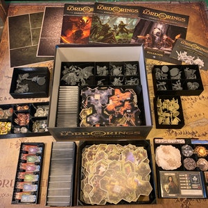 May include: A black and gray organizer box with compartments for storing game pieces and cards. The box is labeled "The Lord of the Rings: Journeys in Middle-earth".