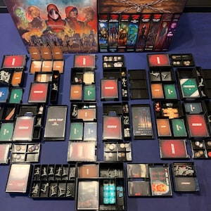 May include: A close-up view of a board game organizer with multiple compartments. The organizer is filled with various game components, including cards, tokens, and miniatures. The organizer is made of black plastic and has a clear lid. The game components are organized in a variety of ways, including by color, type, and size. The organizer is designed to help players keep their game components organized and easy to access.