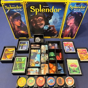 May include: Three Splendor board game boxes featuring illustrated characters and gems, arranged above a black plastic organiser tray containing stacks of game cards, small coloured plastic pagoda tokens, and circular gem-themed tokens in a row.