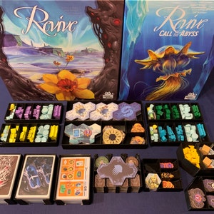 May include: A board game organiser for the game "Revive: Call the Abyss". The organiser is made of black plastic and has multiple compartments for storing the game's components. The organiser is shown with the game's box and components, including tiles, cards, and tokens.