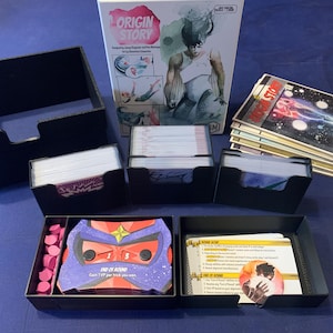 Puede incluir: Un juego de mesa llamado "Origin Story" con varios componentes. El juego incluye una caja, cartas y piezas de juego. La caja presenta una ilustración de personaje. Las cartas están en tarjeteros negros. Las piezas del juego son rosas.