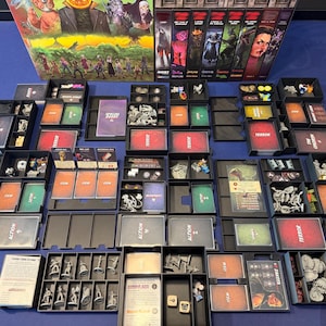 Puede incluir: Un juego de mesa que incluye una caja grande ilustrada, seis cajas de expansión y numerosos organizadores de plástico negro llenos de varios componentes, incluyendo figuras de personajes grises, mazos de cartas y fichas.
