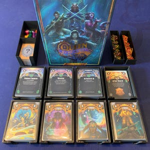 Puede incluir: Un juego de mesa llamado "Queen by Midnight" con una caja azul y morada que presenta a una reina y otros personajes. El juego incluye cartas con ilustraciones de personajes y texto, como "Wildfire" y "Enchanting Growth".