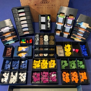 May include: A set of black plastic storage boxes with dividers for organizing the board game "Viticulture: Essential Edition". The boxes contain various components, including cards, tokens, and meeples in different colors. The boxes are labeled with the game's name and the words "Wine Crate".