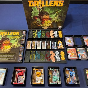 Könnte beinhalten: Das Brettspiel Drillers enthält eine große Spieleschachtel, ein Regelheft und mehrere schwarze Kunststoffschalen mit verschiedenen Spielkomponenten. Dazu gehören kleine farbige Würfel, sechseckige Spielsteine und mehrere illustrierte Kartendecks.