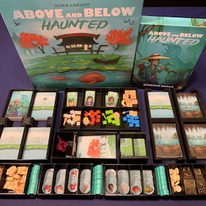 May include: Board game titled "Above and Below Haunted" with a box featuring a Japanese-style scene. The game components are organized in black trays, including cards, tokens, and miniature figures. The color palette includes teal, red, and brown.