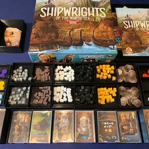 May include: A game board with a variety of game pieces, including wooden cubes, plastic tokens, and cards. The game is called "Shipwrights of the North Sea: Redux".