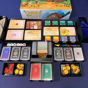 Peut inclure: Un organisateur noir avec des compartiments pour ranger les composants du jeu de société Stardew Valley. L'organisateur comprend des espaces pour les cartes, les dés, les jetons et autres pièces de jeu. L'organisateur est fait de matériaux de haute qualité et est conçu pour garder votre jeu organisé et protégé.