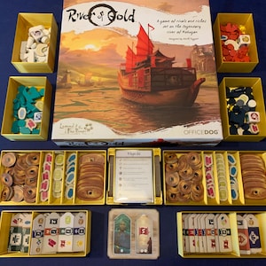 May include: A board game called "River of Gold: Legend of the Five Rings" with a box, game board, and various game pieces. The box art features a red and gold ship sailing on a river.