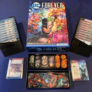 May include: DC Forever board game box set featuring Batman and Joker. Includes card decks, tokens, and game pieces. Two black card holders flank the box. Designed by Damon Stone.