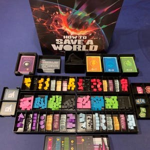 May include: Board game titled "HOW TO SAVE A WORLD" with various game components. The game includes cards, wooden blocks, and other game pieces in a variety of colors, including yellow, pink, green, and blue. The game is set on a blue surface.